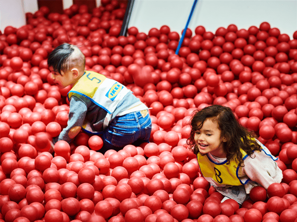 two children are playing in the Smaland play corner among red balls.