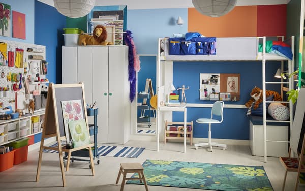 Two children in a green and white kids’ bedroom with bunk beds and wall-mounted bookshelves.