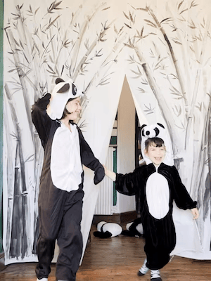 Two children in panda bear costumes take a bow in front of a stage curtain made from a decorated BJÄRSEN shower curtain.