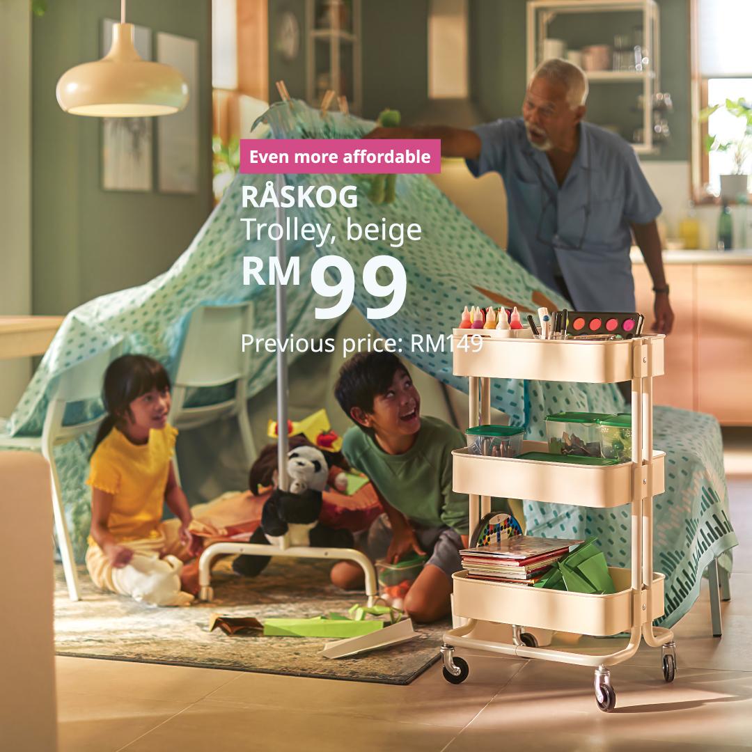 Two children play in a homemade blanket fort while an adult joins in, with a three-tier trolley nearby keeping art supplies, books and toys organised and within easy reach.