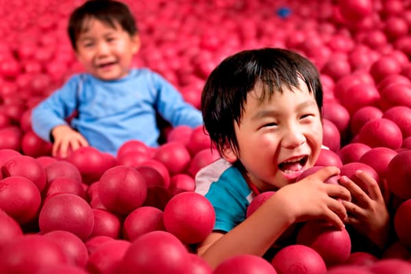 two children playing in a ball pit with red balls