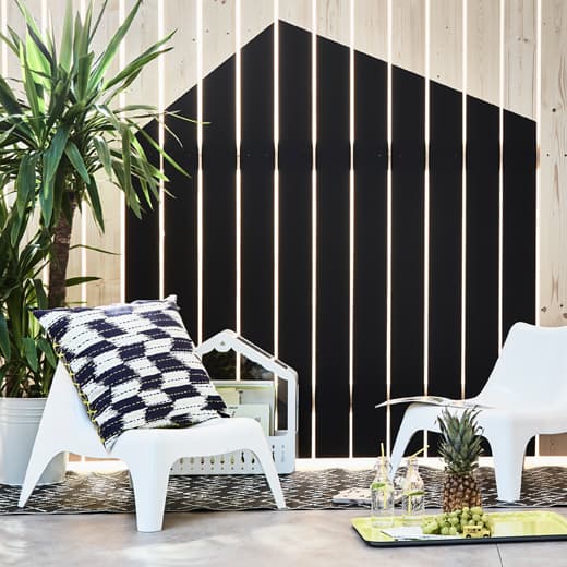 Two children’s easy chairs arranged by a fence that’s painted to look like a house 