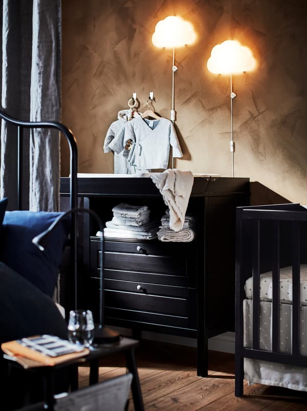 Two cloud-shaped UPPLYST LED wall lamps above a black SUNDVIK wooden changing table with two drawers beside a crib.
