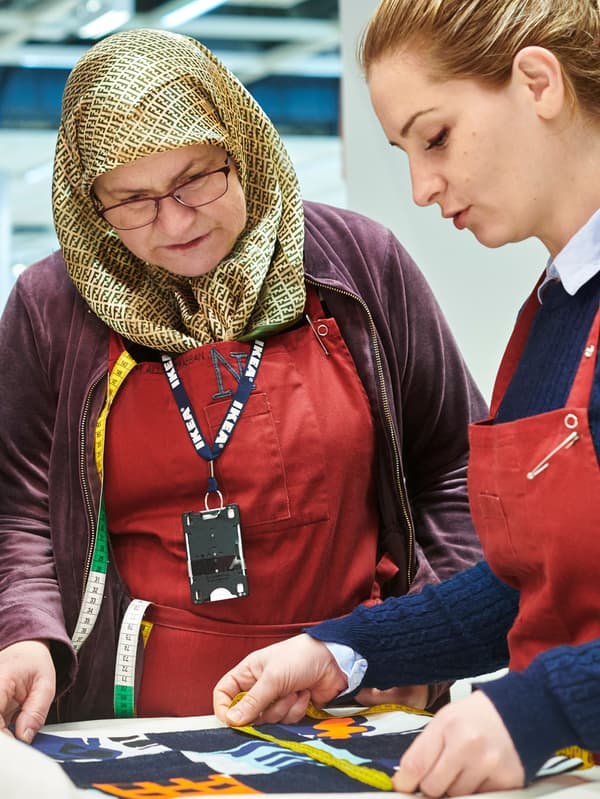 Two co-workers from Yalla Trappan sewing studio in the Malmö IKEA store in Sweden, measuring some fabric.