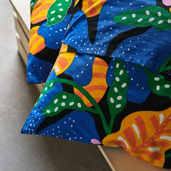 Two cushions with colourful MÄVINN covers featuring a bold abstract pattern in blue, green, yellow and orange.