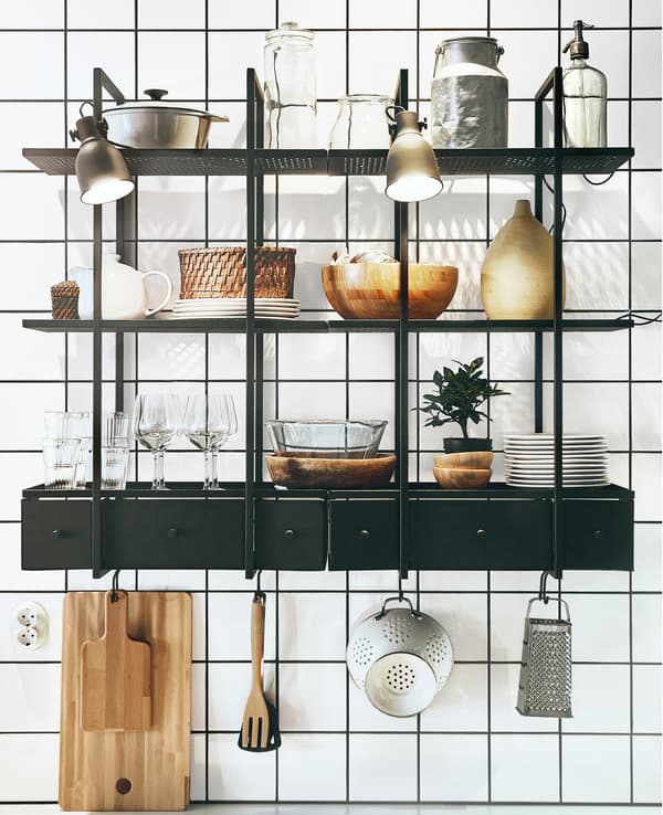 Two dark metal open shelving units with plates, glasses and kitchen stuff on a white tile wall.