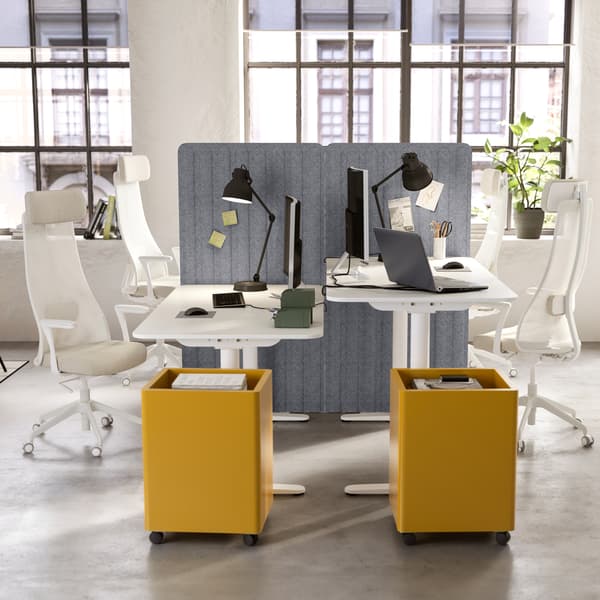 Two desks standing opposite each other, white storage cabinets on wheels, beige/white ergonomic chairs, black desk lamps.