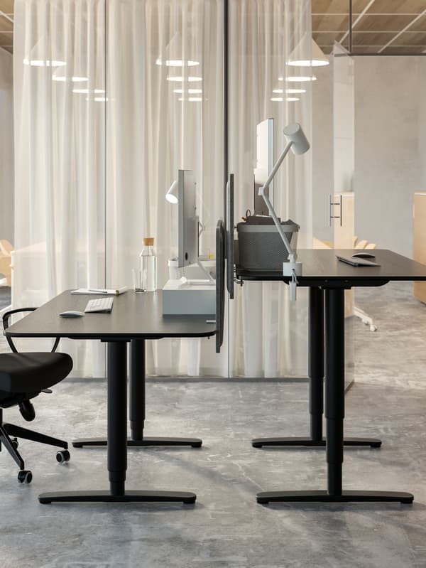 Two different-height, facing, black-stained-ash-veneer-and-black BEKANT sit-stand desks in a light office interior.