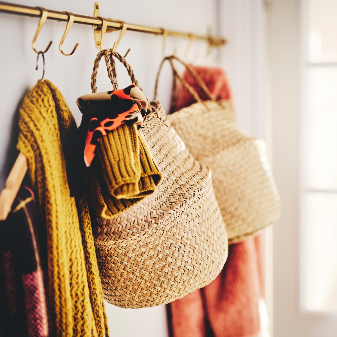 Two FLÅDIS baskets stuffed with clothing items and two scarfs on a hanger, hanging on gold-tinted hooks.