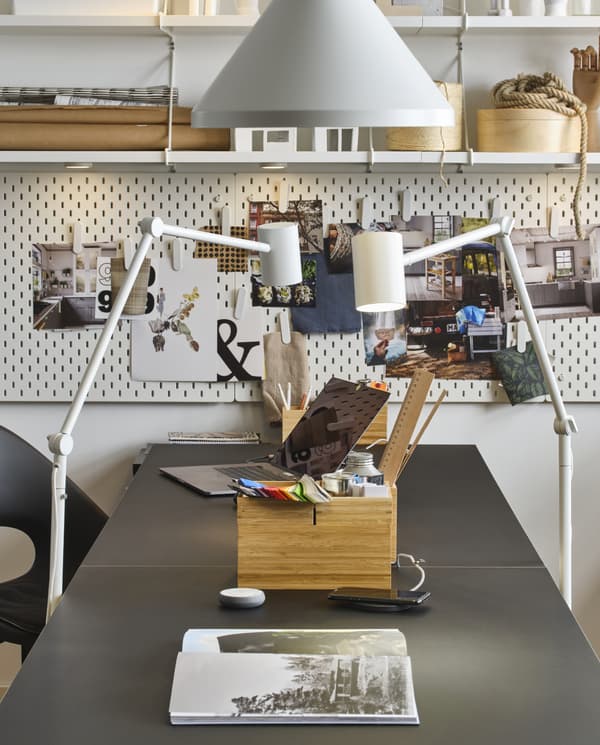Two floor lamps and one pendant lamp in white, a black table, a laptop, a box in bamboo and shelves and pegboards in white.