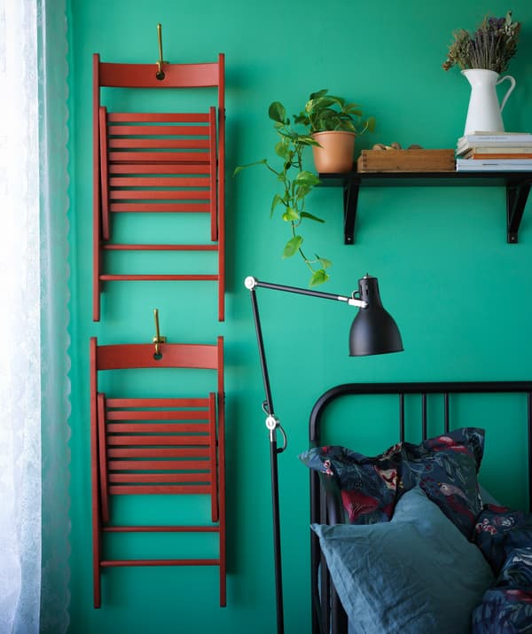Two foldable chairs hanging on a wall beside a bed.