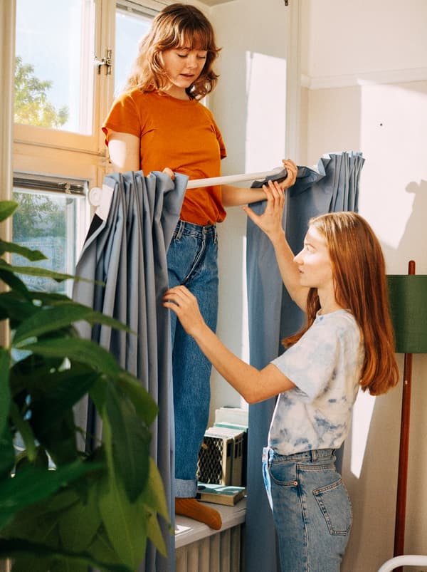 Two girls getting ready to hang curtains using a shower curtain rod.