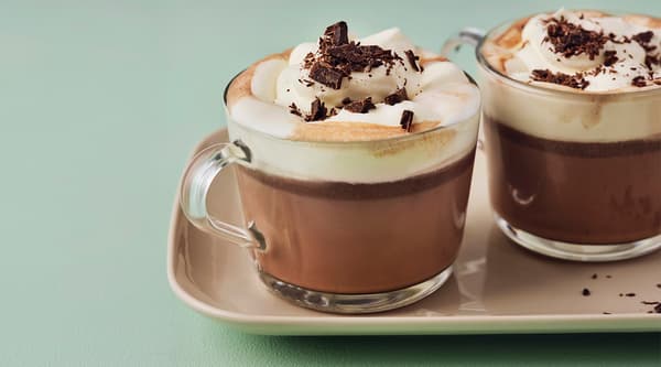 Two glass mugs filled with hot chocolate and topped with whipped cream and chocolate shavings.