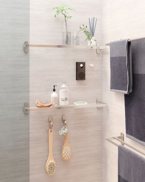 Two glass shelves are mounted on a wall and between them a white knob where a small portable Bluetooth speaker is hanging.