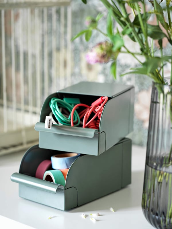 Two green bins on a desktop with rolled up cords inside.