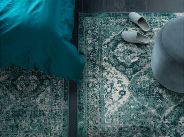 Two green rugs in an oriental-vintage expression are placed next to each other on a bedroom floor, one is next to the bed.