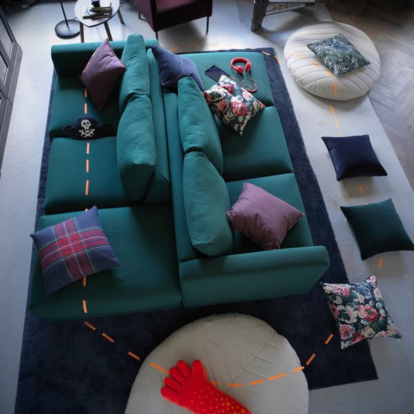 Two green VIMLE sofas back to back, with cushions and pouffes scattered around the floor and marked with a tape trail.