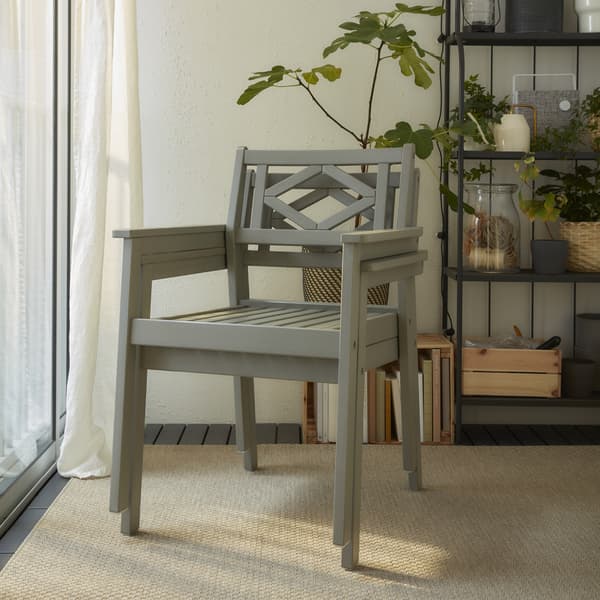 Two grey chairs with armrests are stacked. They stand on a beige rug, and a grey shelving unit with plants stands behind.