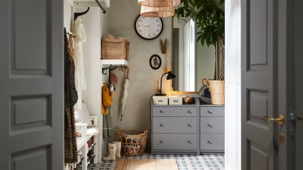 Two grey HAUGA chests of 3 drawers stand in a hallway with a RÅMEBO mirror and a large wall clock on the wall.