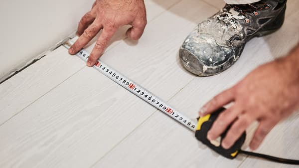 Two hands are holding a measuring tape on a white wood floor.