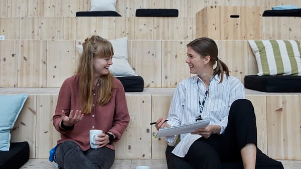 Two IKEA co-workers dressed in casual clothes enjoying a chat and coffee while sitting on wooden stairs.