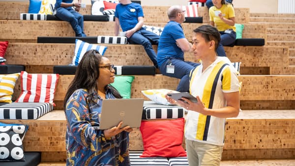 Two IKEA co-workers dressed in casual clothes enjoying a chat and coffee while sitting on wooden stairs.