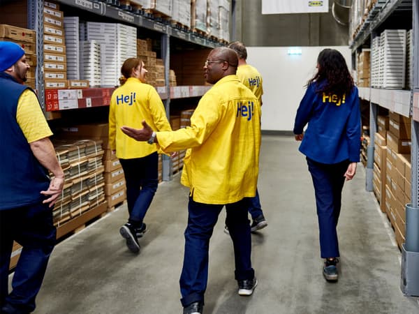 Two IKEA co-workers leaning over a wooden frame. They are both wearing lanyards and are smiling.