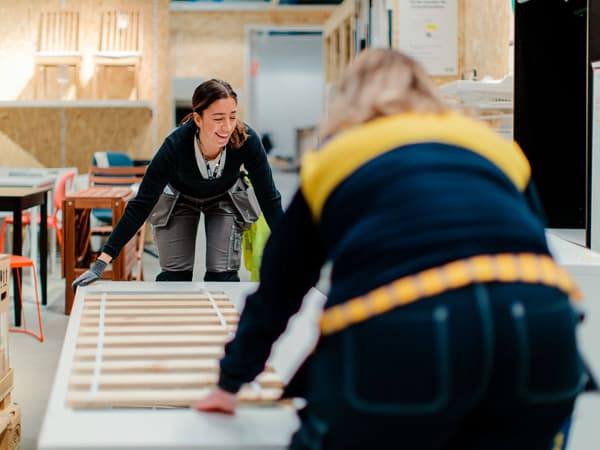 Two IKEA co-workers moving a mattress inside an IKEA store.