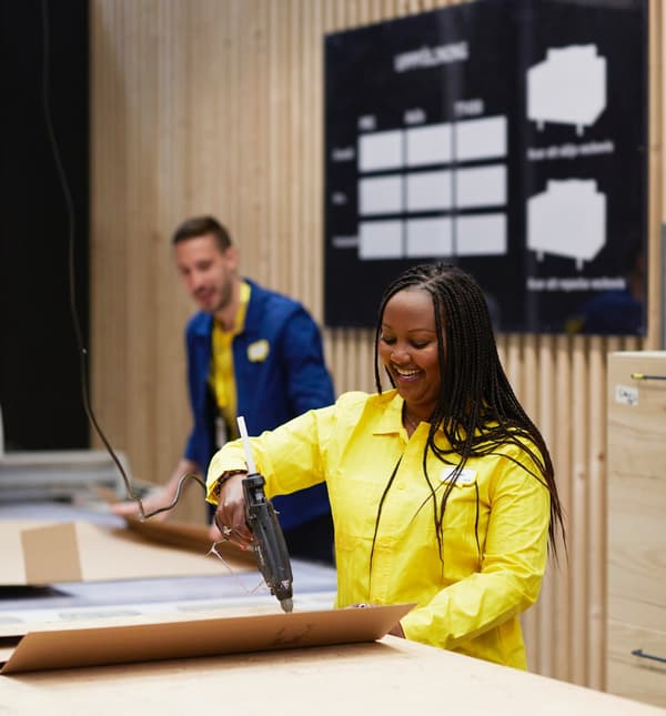 Two IKEA co-workers, one in a yellow top and one in a blue top, packing items in cardboard packaging.