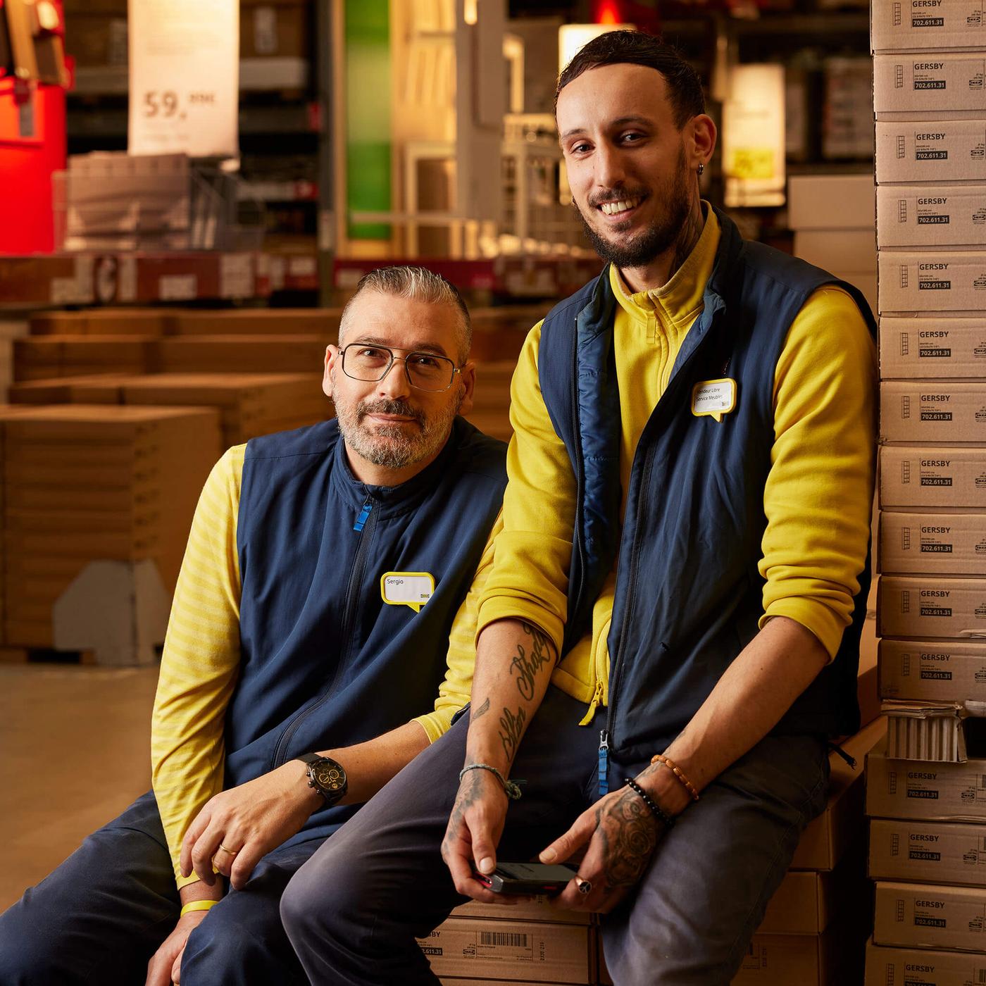 Two IKEA co-workers sitting in a self-serve warehouse smiling.