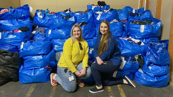 Two IKEA co-workers smiling at the camera in front of a large amount of IKEA bags filled with donations.