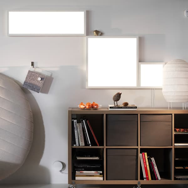 Two IKEA FLOALT LED panels in white on a wall above an open storage cabinet.