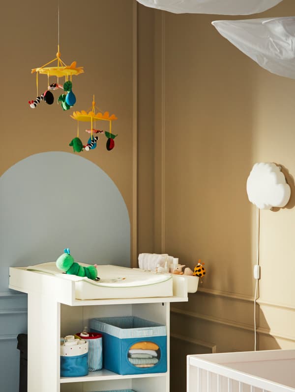 Two IKEA KLAPPA mobiles above a changing table with baby changing products, a soft toy caterpillar and a wall night light.