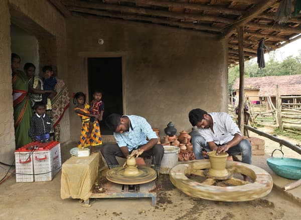 Two Indian potters working on their potting wheels while being observed by other villagers.