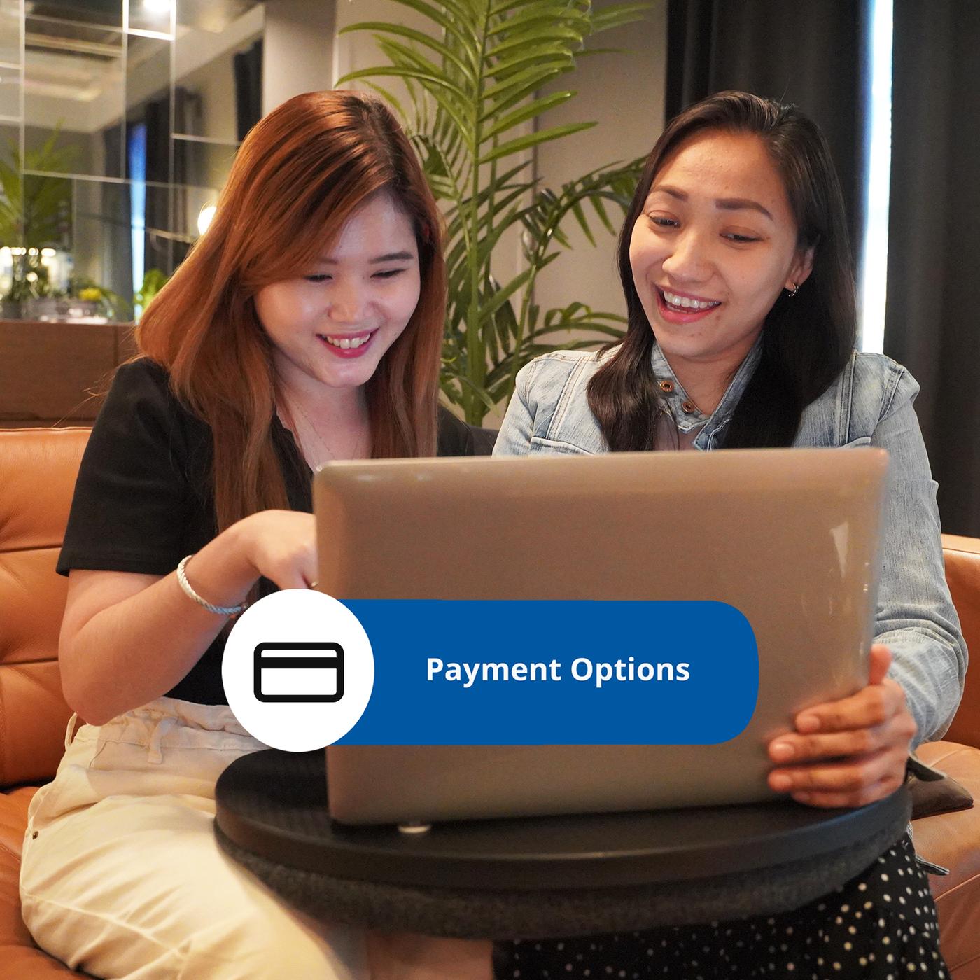 Two individuals are sitting on a couch, discussing payment options while looking at a laptop in a cozy, modern setting.