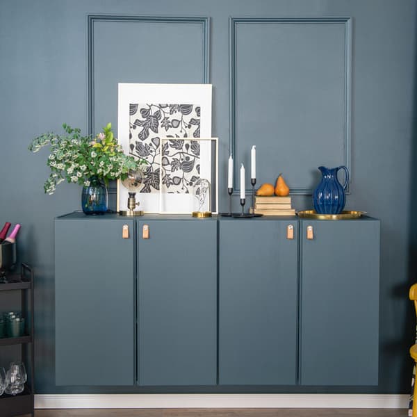 Two IVAR cabinets on a wall are painted blue and have leather handles. Several items are placed on top of the cabinets, such as candles, a picture frame, and a plant in a vase.