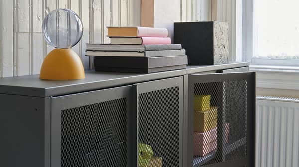 Two IVAR mesh cabinets in grey featuring see-through metal mesh in the doors, propped with yellow and pink objects.