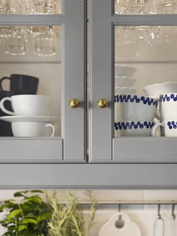 Two kitchen cabinets with glass doors and grey frames, containing a selection of coffee cups and glasses.