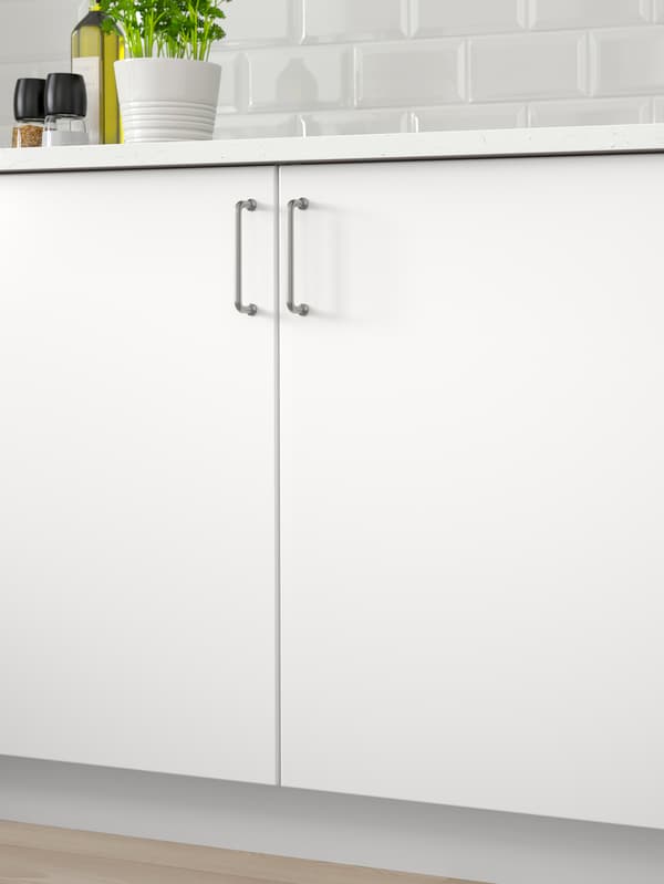 Two kitchen cabinets with white fronts and a white worktop with a green plant, oil and spice mills on top.