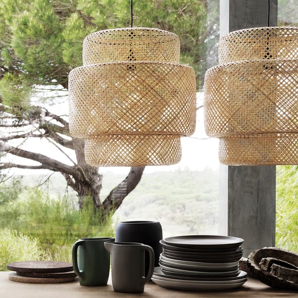 Two large SINNERLIG bamboo pendant lamps hung above a table informally set with rustic ceramic dishes.
