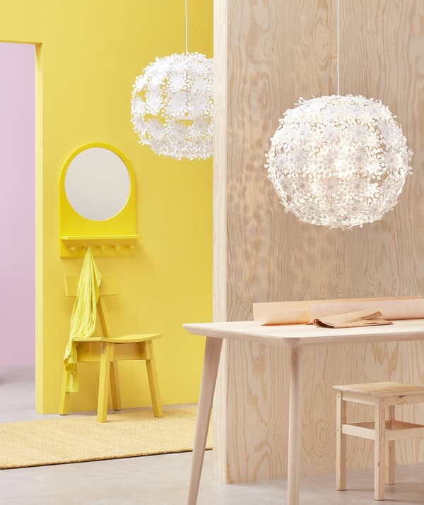 Two large white pendant lamps with floral design hanging in a pink, yellow and light wood room.