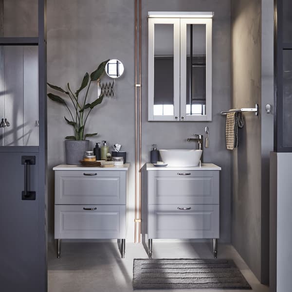 Two light gray bathroom sink cabinets and drawers with a wall mounted cabinet above, against a gray wall.