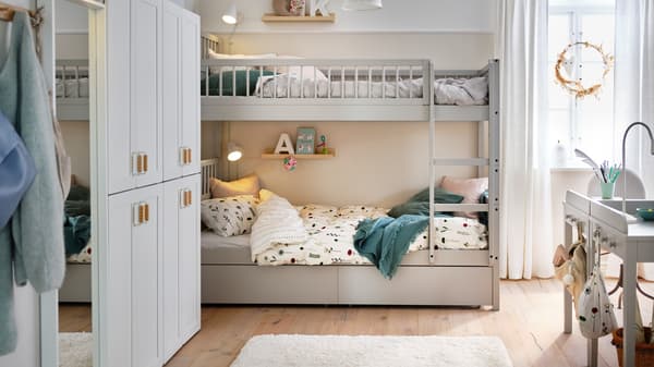 Two light grey SMYGA beds as a bunkbed in a bedroom with wall lamps and a shelf by each bed. A cream rug is on the floor.