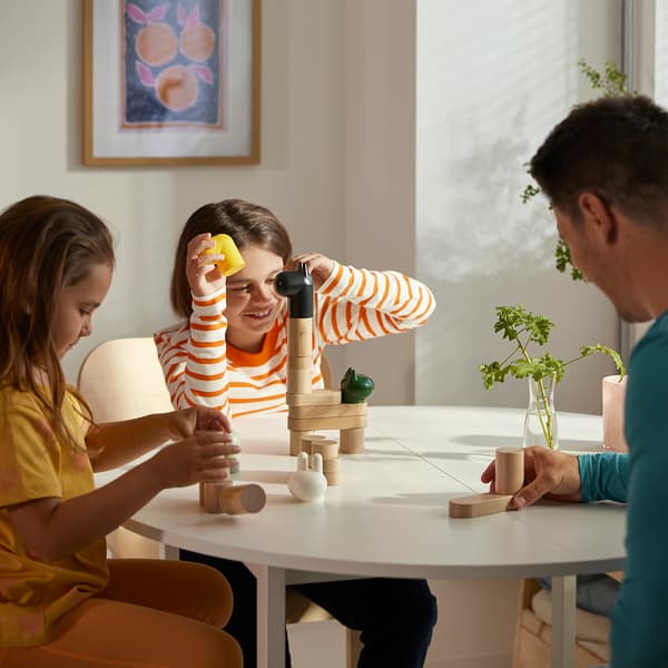 two little girls and their father play with a set of wooden toys 