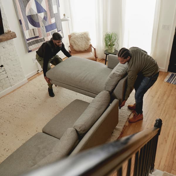 Two men lifting a light grey sofa.