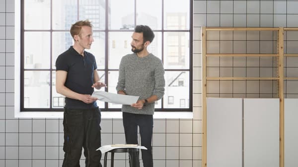 Two men standing in a bathroom and discussing installation.