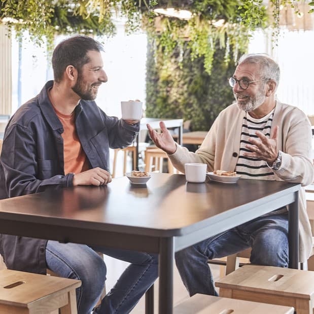 Two men talking to each others in front of a cup of coffee 