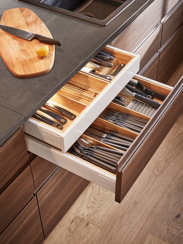 Two open dark brown kitchen drawers with lighting storing cutlery inside.