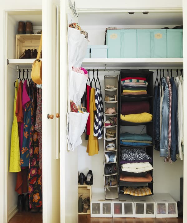 Two open in-built wardrobes with hanging storage and boxes filled with colourful clothes and shoes.