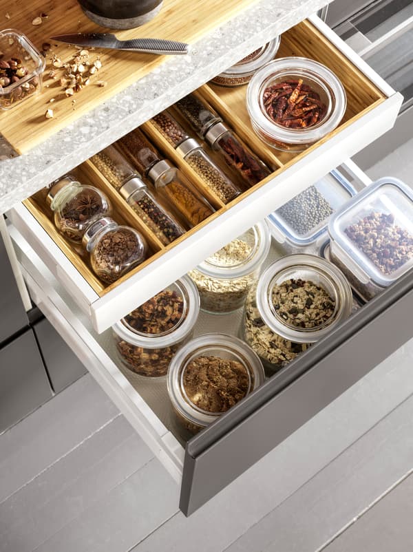 Two open kitchen drawers with grains in glass jars and spices neatly organised inside a VARIERA cutlery tray in wood.